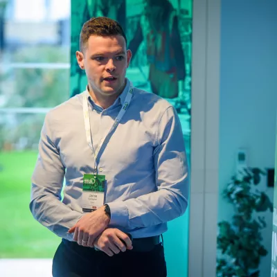 A male in a business shirt with an event lanyard talking.
