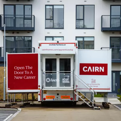 A truck with Cairn branding and steps up to it parked in front of a white building.