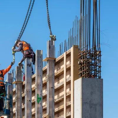 A person in a high vis jacket and hard hat passes the hook from a chain to another person, working on top of scaffolding.