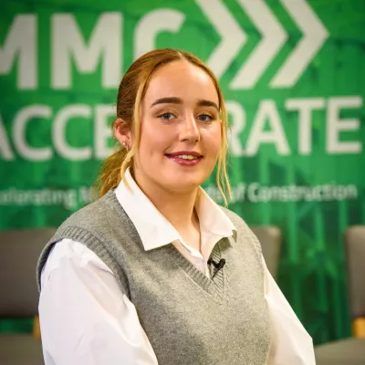A young female wearing a grey wool vest and white business shirt smiling.
