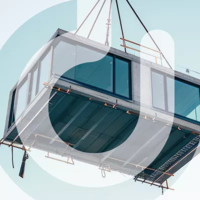 A modular building unit being hoisted with chains by a crane.