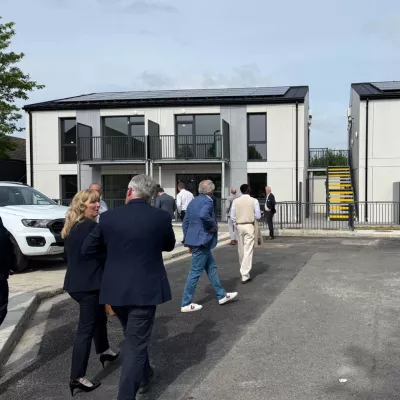A group of people talking walk through a car park towards a modern house.