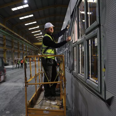 Person in high-vis working on a window module inside a large factory, standing on a mobile platform.