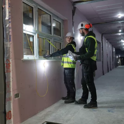 Two people in high-vis vests inspecting a window inside a construction unit