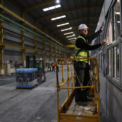 A male with a high vis vest and hard hat stands on a scissor lift to fit a window.