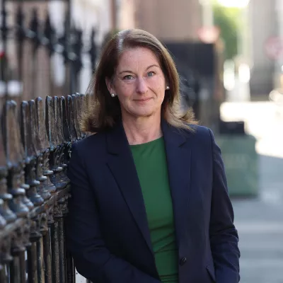 Person in a green dress and blue jacket standing outside a building.