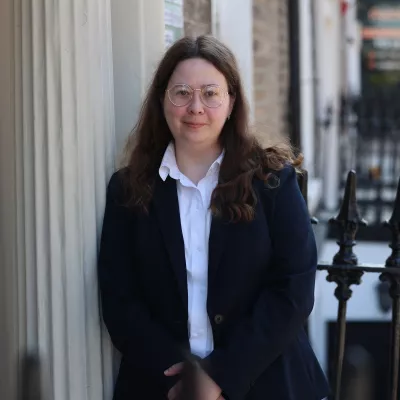 Headshot of a person in a blue jacket standing outside a building.