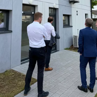 A group of people in business shirts and suits gather outside a modern house.