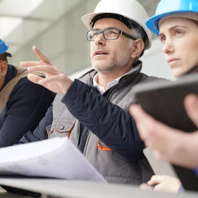 A group of people in hard hats review building plans on large paper charts.