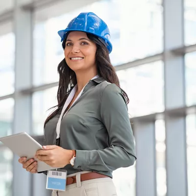 Person wearing a blue hard hat and holding a tablet, standing in a bright modern building.