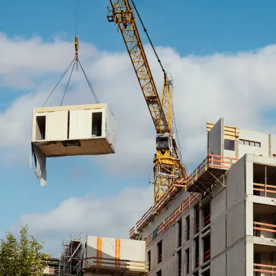A crane lifts a modular building unit across a construction site.