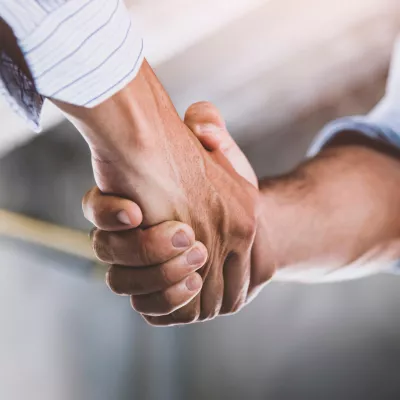 A person in a business shirt shakes hands with a person in a business shirt and high vis vest.