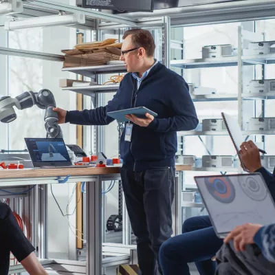 man displaying a robotic arm to a group of people in a classroom setting
