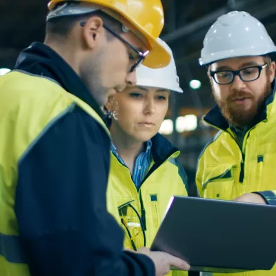 A group of people in hard hats and high vis vests read from a tablet screen.