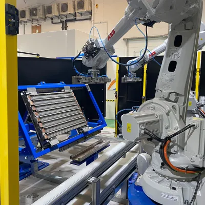 A robotic arm inside a safety enclosure working on a blue metal fixture holding a mechanical component in a manufacturing or training facility.