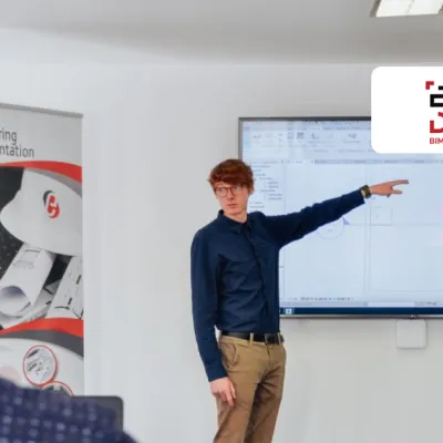 A person is standing next to a screen, pointing at a slide during a training session in a classroom.