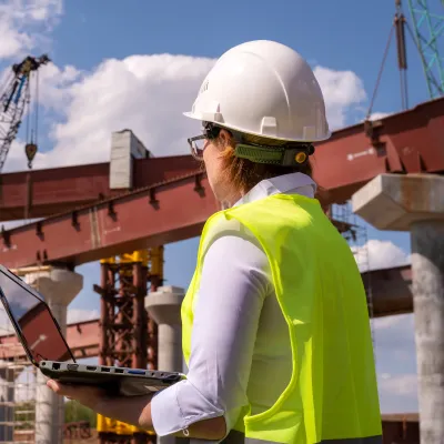 A construction worker wearing a high-visibility vest stands in front of steel structures.