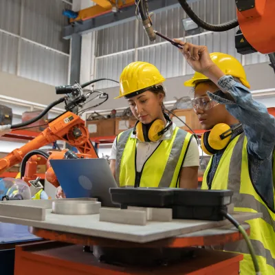 Two workers wearing high-visibility vests and hard hats are working with robotics.