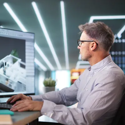 Architect working on 3D building model using multiple computer monitors.