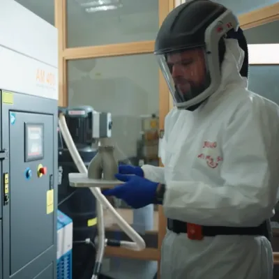 Technician in protective gear operating a Renishaw metal 3D printer inside a laboratory or manufacturing facility.