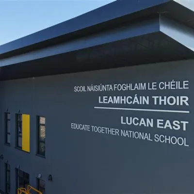 A modern two-storey school building with dark grey and white exterior panels, yellow accent features, and large windows.