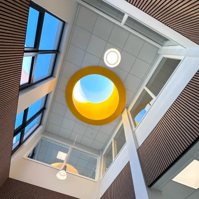 A bright, modern school interior with large windows, a central skylight featuring a yellow circular frame