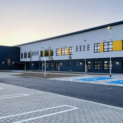 A modern two-storey school building with dark grey and white exterior panels, yellow accent features, and large windows.