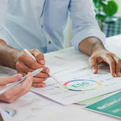 Close-up of hands reviewing architectural or technical documents with charts and drawings on a desk, suggesting a collaborative planning or design meeting.