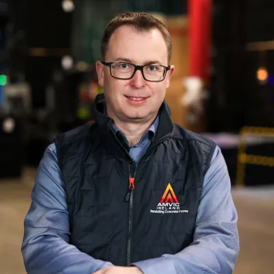 Person wearing glasses and a vest with Amvic Ireland logo, leaning on form blocks.