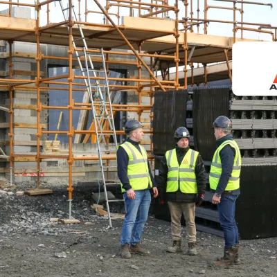 Three construction workers in helmets and safety vests discussing at a building site with scaffolding
