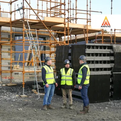 Three construction workers in helmets and safety vests discussing at a building site with scaffolding