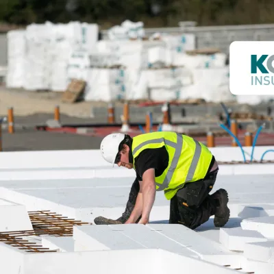Construction worker in a high-visibility vest and hard hat installing insulation panels on a building site.