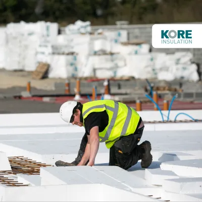 Construction worker in a high-visibility vest and hard hat installing insulation panels on a building site.