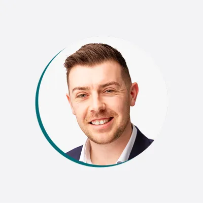 a person in a suit jacket and white shirt, smiling at the camera against a light background.