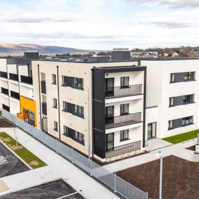 Modern three-storey apartment building with balconies and a mix of white, grey, and yellow facade panels.