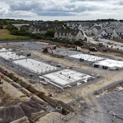 Large construction site with multiple building foundations at different stages of installation, surrounded by machinery and housing in the background.