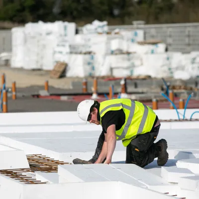 Construction worker in a high-visibility vest and hard hat installing insulation panels on a building site.