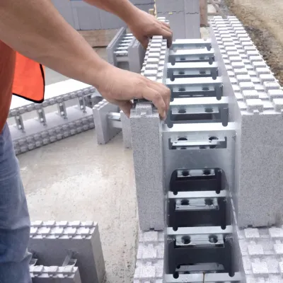 Close-up of a worker’s hands placing interlocking concrete blocks with steel reinforcement on a construction site.