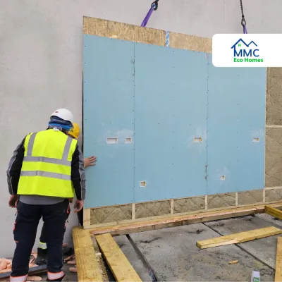 Workers in safety gear installing a large prefabricated wall panel on a construction site
