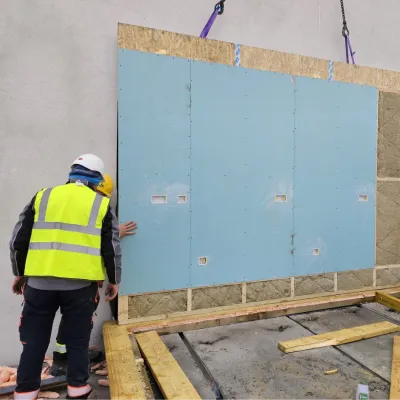 Workers in safety gear installing a large prefabricated wall panel on a construction site