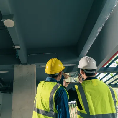 Two construction workers in safety vests and helmets inspecting ceiling installations