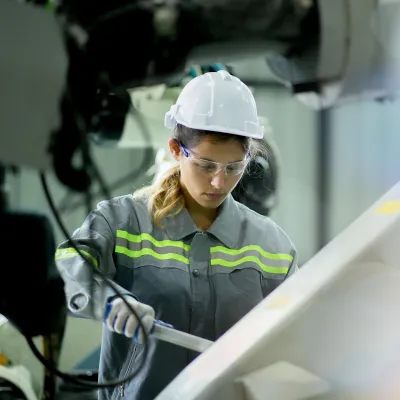 Person wearing a hard hat, safety glasses, and protective clothing operating equipment in an industrial setting.