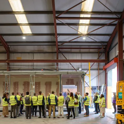 Group of workers in high-visibility vests gathered inside a large industrial warehouse with stacked containers.