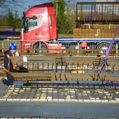 Construction workers assembling rebar on a site with a red truck visible in the background.