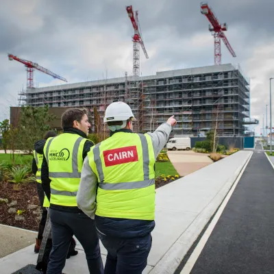 Construction workers in high-visibility vests overlooking a building site with cranes and scaffolding.