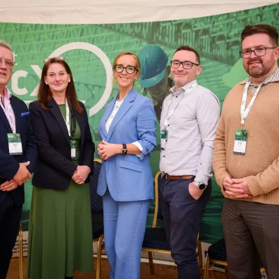 Five people standing together in front of a green Skillnet MMC Accelerate event banner, facing the camera and smiling.