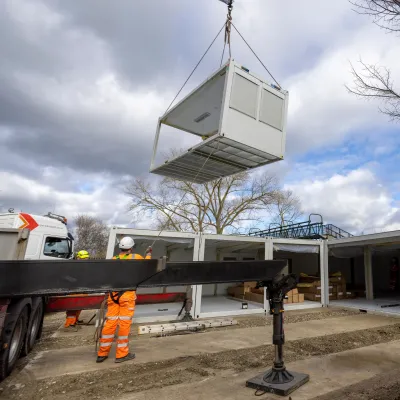 A modular building unit being lifted by a crane at a construction site.