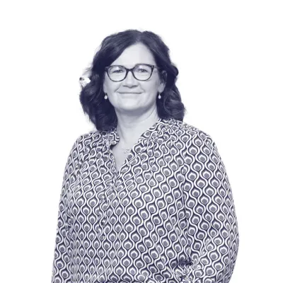 Person wearing glasses and a patterned blouse, smiling against a plain light background.
