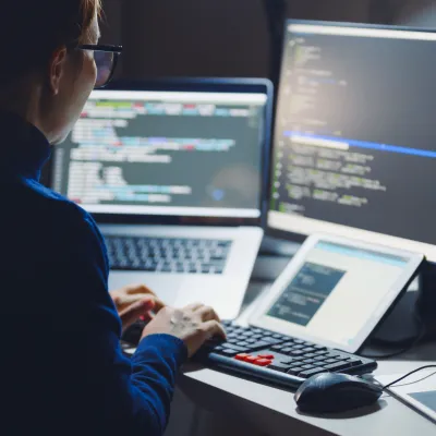 Person working at a desk with multiple screens showing code and data.