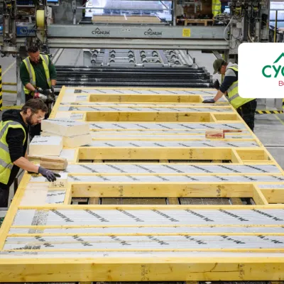 Workers in high-visibility vests assembling insulated timber wall panels inside a modern offsite construction factory.